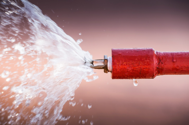 Close-up of a red fire sprinkler pipe actively discharging water, symbolizing emergency fire suppression in action