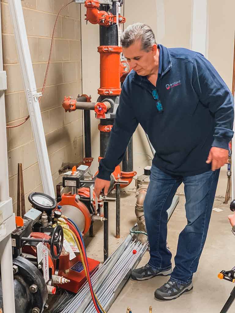 Technician adjusting fire protection equipment with gauges and valves in a mechanical room