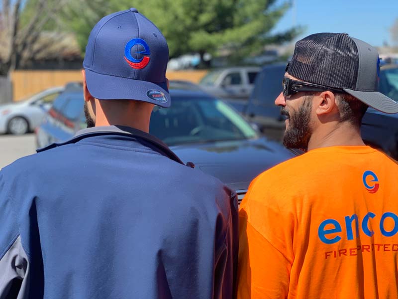 Two Encore technicians from behind, one wearing a blue jacket and cap, the other in an orange shirt