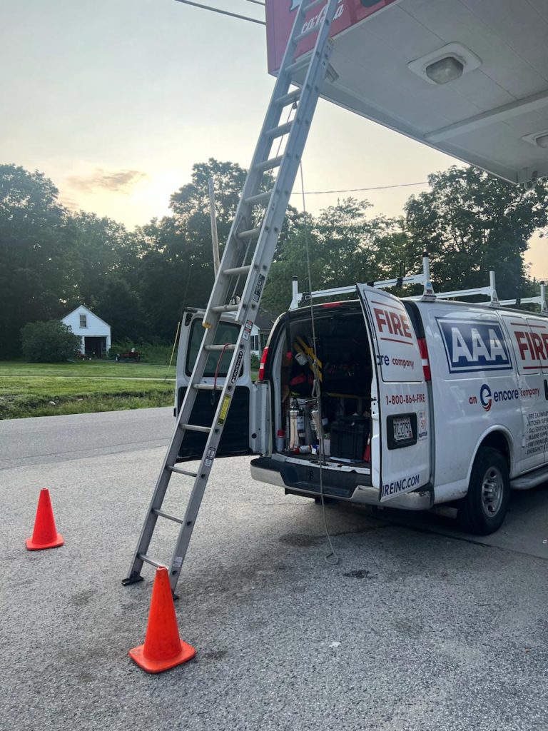 AAA Fire Services van with an extended ladder and safety cones, parked at a gas station during sunrise