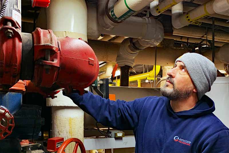 Technician inspecting a red valve part of a fire suppression system in a mechanical room