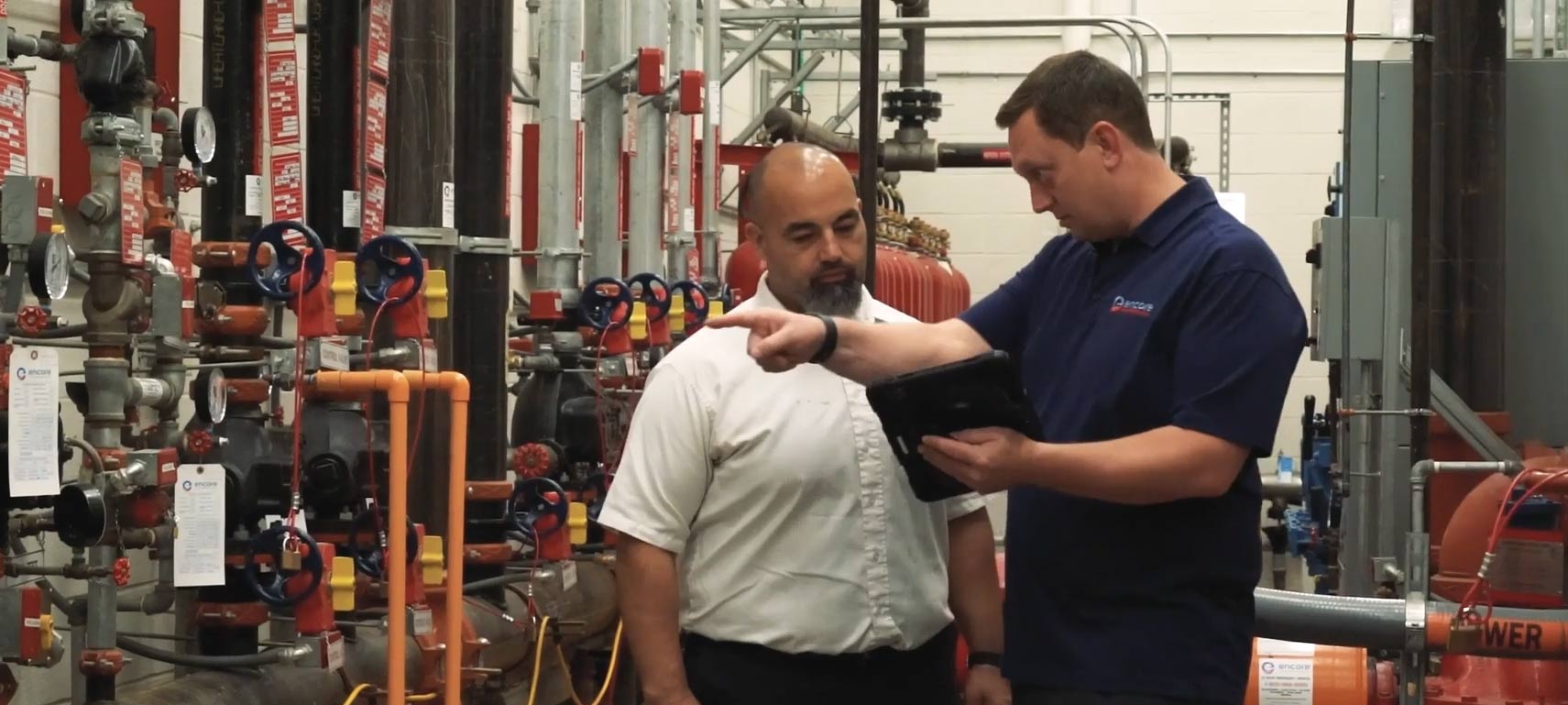Two technicians inspecting fire protection systems with gauges and valves in an industrial setting.