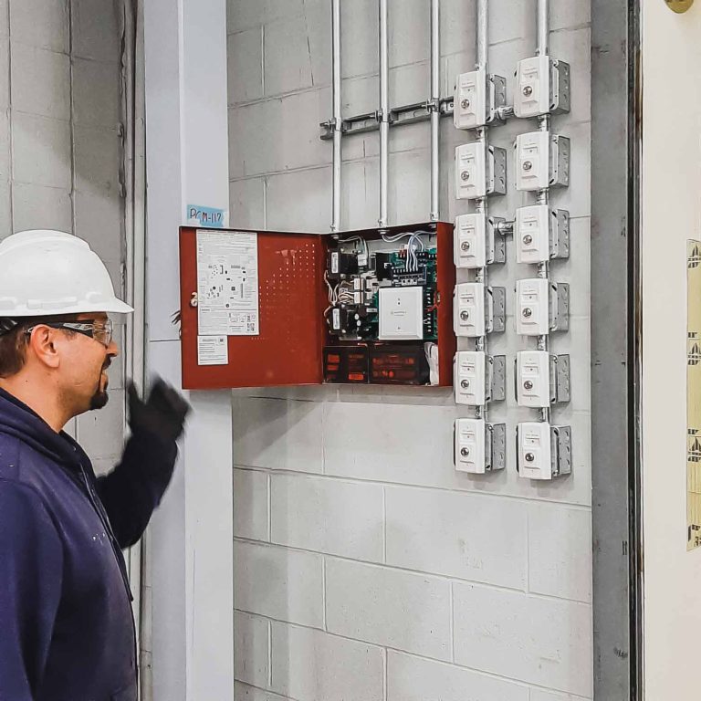 Technician in a hard hat inspecting a fire protection control panel mounted on a wall