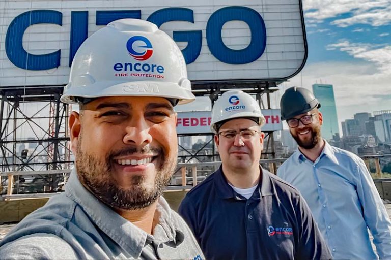 Three Encore employees in hard hats in front of CITGO sign in Boston MA