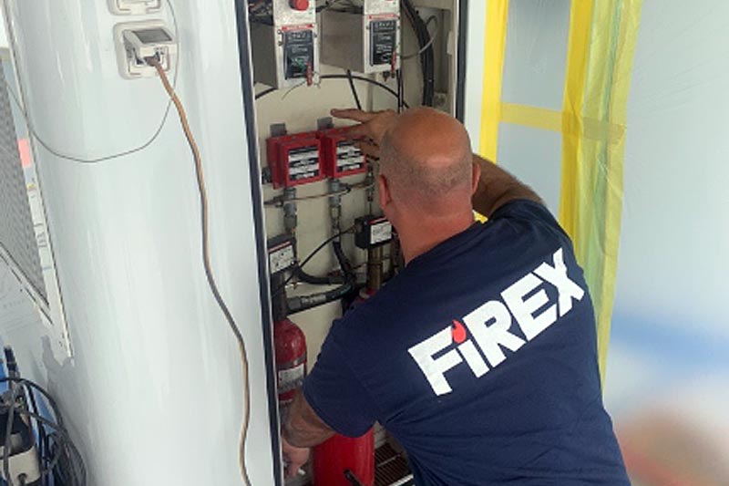 Technician in a FiREX shirt working on a marine fire suppression system.