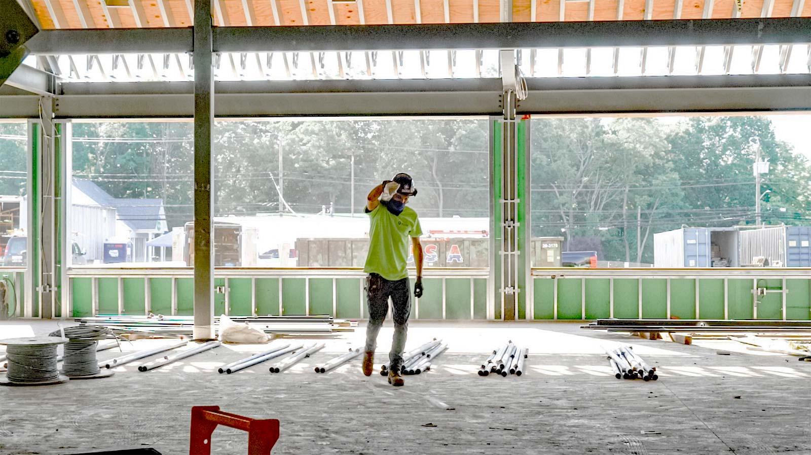 Construction worker in a neon shirt and hard hat walking through a large open construction site