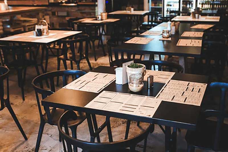Empty restaurant dining area with tables set with menus and small potted plants